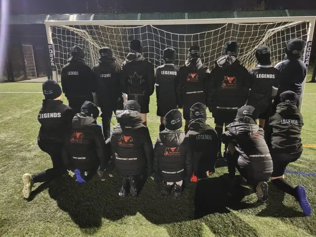 Breightmet United Youth Football Team on a training ground on astro turf, all dressed in black coats and black hats