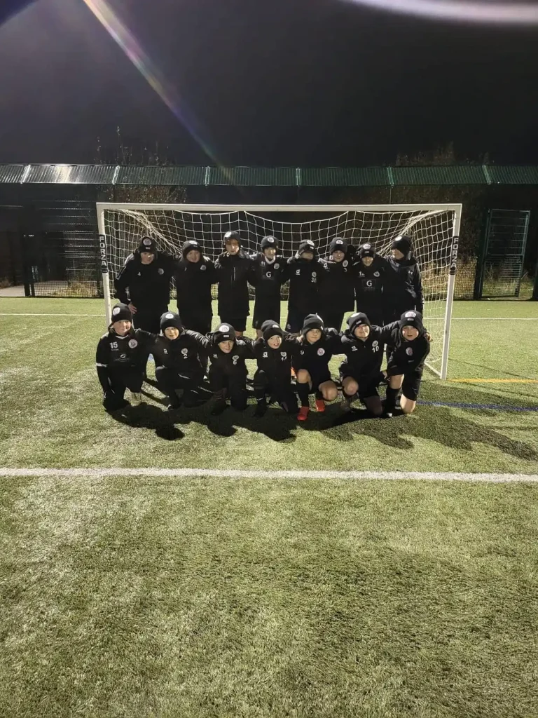 Breightmet United Youth Football Team on a training ground on astro turf, all dressed in black coats and black hats